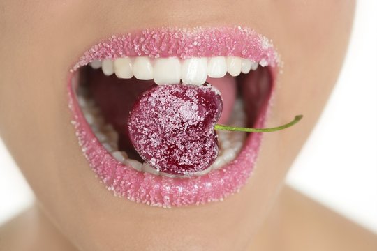Cherry with sugar between woman teeth