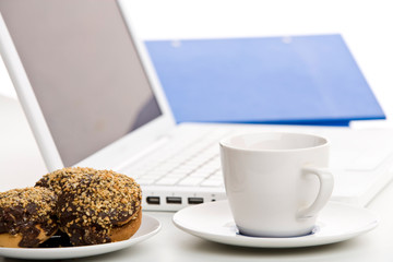 Desk with laptop computer, cakes and cup of coffee