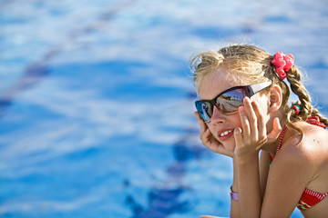 Child girl in red bikini and glasses near blue swimming pool.