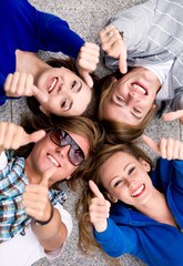 Four young friends lying down showing thumbs up sign