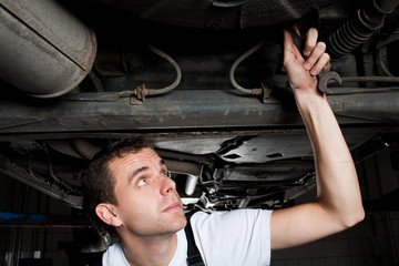 closeup of mechanic working below car with wrench