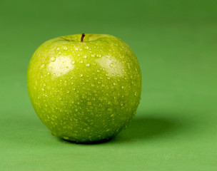 Green apple with water drops on green background
