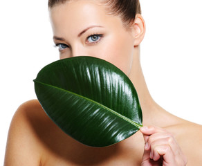 woman with healthy skin covering her face by fresh green leaf