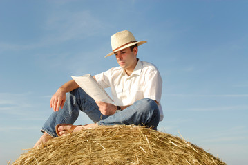 jeune homme avec chapeau lisant sur un ballot de paille