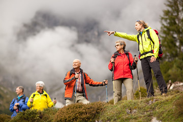 young female hiking guide showing senior group surrounding mount - obrazy, fototapety, plakaty