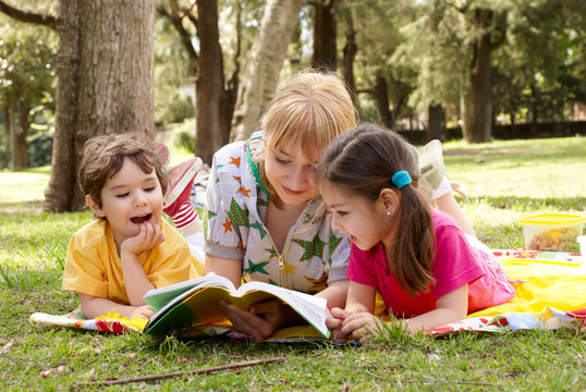 Elder sister reads to children of the book on a glade in park