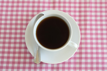 A cup of coffee on a pink and white table cloth.