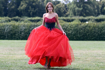 Fototapeta premium Smiling woman in a red dress walking on meadow in park
