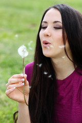 young woman blowing on the dandelion .