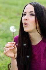 young woman blowing on the dandelion .