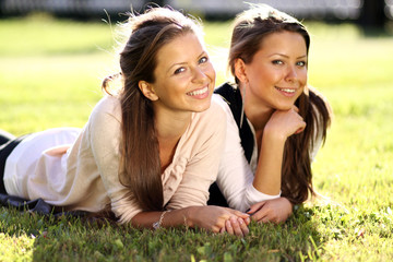 Young beautiful twins of sister lays on green field