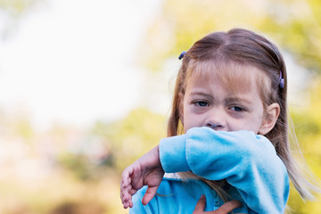 Little girl coughing or sneezing into her elbow.