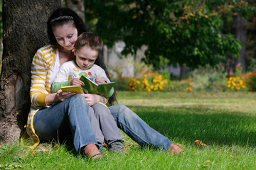 mother and son reading book in autumn park