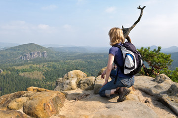 Frau mit Rucksack hockt auf Felsen im Elbsandsteingebirge