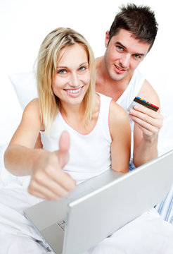 Couple in bed buying on-line with thumb up