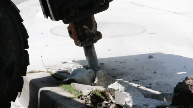 Jackhammer mounted on to a skid steer loader breaking concrete