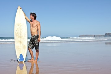 Surfer and his surfboard at the beach ready to surf