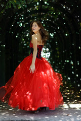 Fototapeta premium woman in a red dress walking in alleyway in park