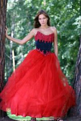 Fototapeta premium A beautiful woman in a red dress standing among trees in park