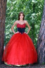 A beautiful woman in a red dress standing among trees in park