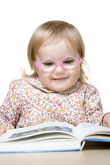 Smiling baby girl with glasses reading book