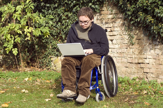 junger Rollstuhlfahrer. Student mit Laptop im Park