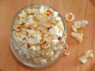 Popcorns spilling from bowl made of glass on wooden background