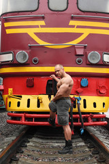 shirtless athlete stands on railroad against locomotive
