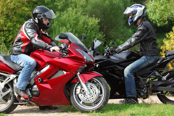 two motorcyclists standing on country road, side view
