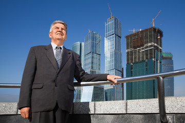 smiling senior man in suit near skyscrapers construction