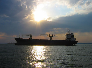 Dry cargo ship silhouette in sunlight going through clouds