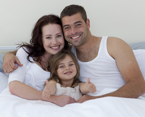 Happy young family in bed with thumbs up