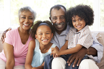 Grandparents With Grandchildren Relaxing On Sofa At Home Togethe