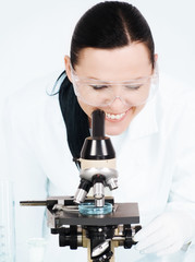 smiling brunette female researcher working on microscope in labo
