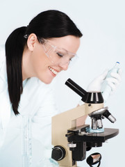 smiling brunette female researcher working on microscope