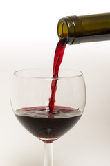 Bottle's neck and wine glass with streaming red wine