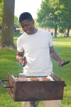 Teen Boy Grilling Hamburgers At A Park