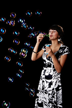 The girl blows soap bubbles on a black background