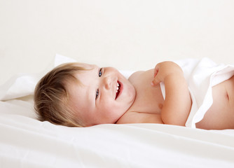 Fototapeta premium baby lying on white sheet smiling