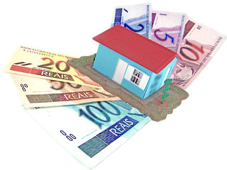little model house over a lot of brazilian real banknote
