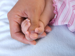 Babyhand umfasst den Daumen von Mutters Hand