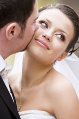 portrair of beautiful smiling bride and groom kissing her