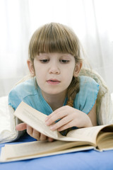 little girl reading a book lying in bed