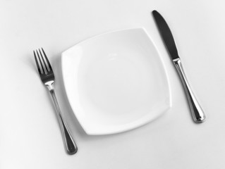 Place setting for one person. Knife, square white plate and fork