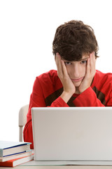 Tired teenage boy sitting behind desk using laptop computer