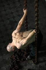Muscular man  leaning over and pulling on chains.