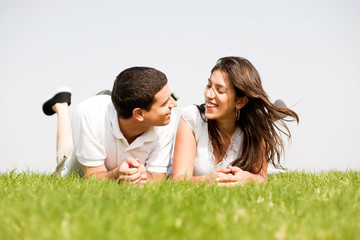 young couple smiling by laying down in a green grass field