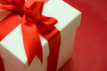 white gift box with a red ribbon and bow on red background