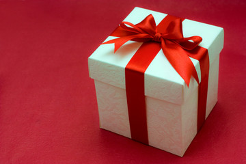 white gift box with a red ribbon and bow on red background
