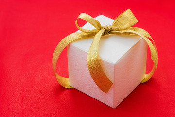 white gift box with a golden ribbon and bow on red background